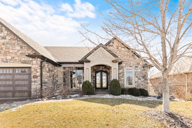 french country inspired facade featuring stone siding, roof with shingles, an attached garage, french doors, and a front yard