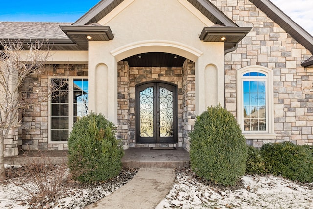 view of exterior entry featuring stone siding, roof with shingles, and stucco siding