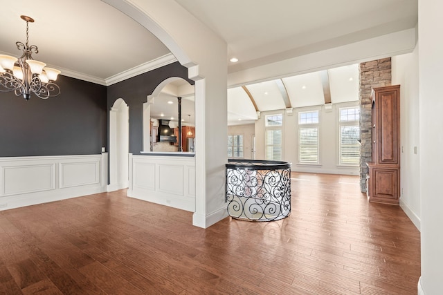 spare room with a wainscoted wall, arched walkways, wood finished floors, and a chandelier