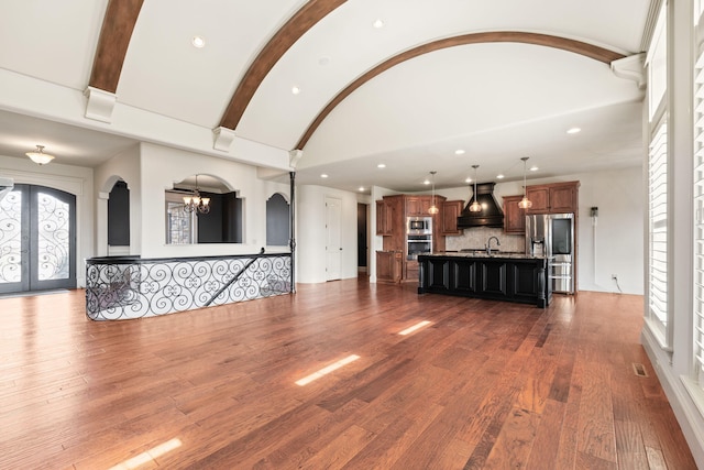 unfurnished living room featuring arched walkways, dark wood-style floors, vaulted ceiling with beams, an inviting chandelier, and french doors