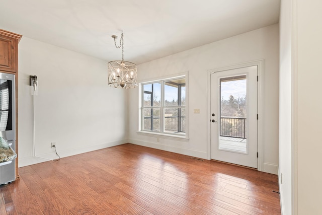 unfurnished dining area with baseboards, light wood-style flooring, and a notable chandelier