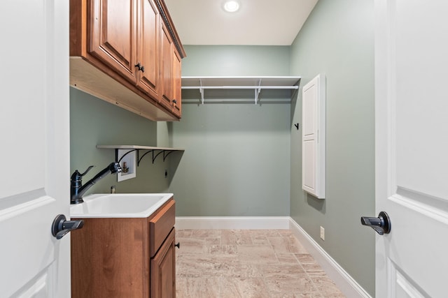 washroom featuring cabinet space, baseboards, hookup for a washing machine, stone finish flooring, and a sink