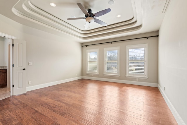 spare room featuring ceiling fan, a tray ceiling, light wood-type flooring, and baseboards