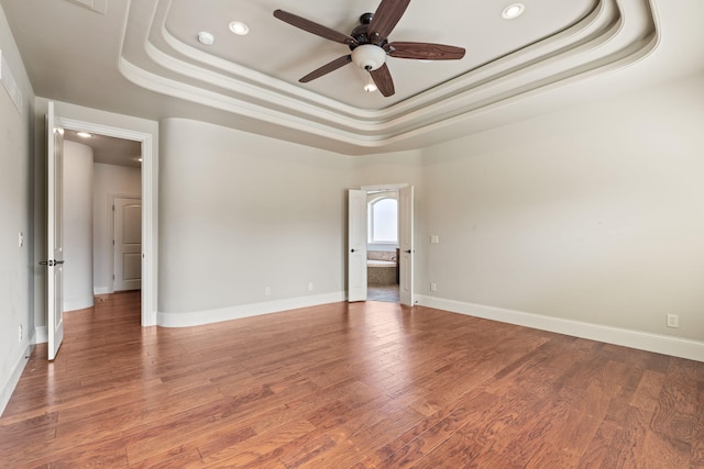 spare room with baseboards, a tray ceiling, ceiling fan, and wood finished floors