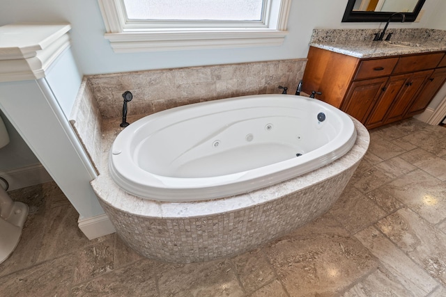 bathroom featuring a whirlpool tub, stone finish flooring, and vanity