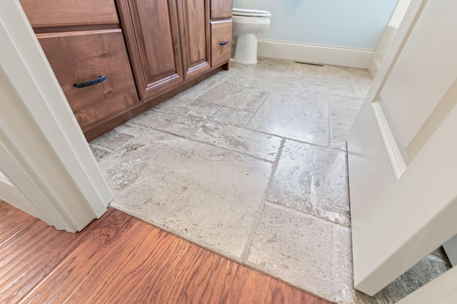 room details featuring toilet, visible vents, baseboards, and wood finished floors