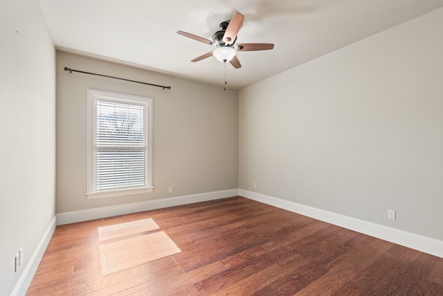 empty room with visible vents, wood finished floors, a ceiling fan, and baseboards