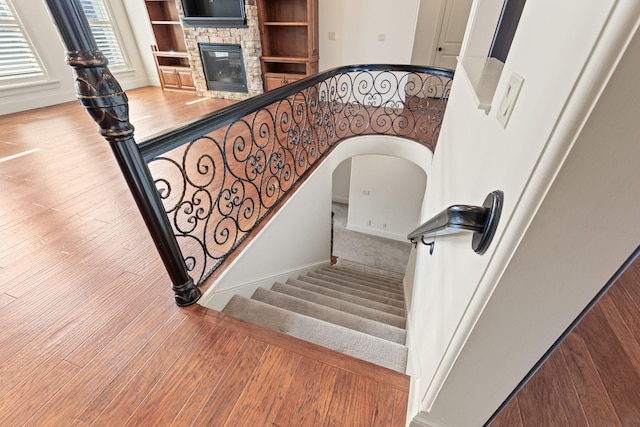 stairway featuring a fireplace, arched walkways, and wood finished floors