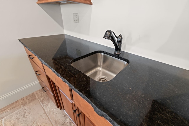 interior details with brown cabinetry, dark stone countertops, a sink, and baseboards