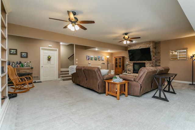 living room with ceiling fan, a stone fireplace, light colored carpet, baseboards, and stairway