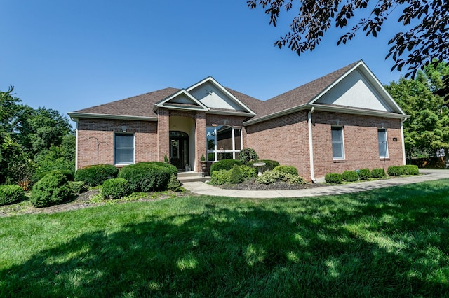 view of front facade with a shingled roof, a front lawn, and brick siding