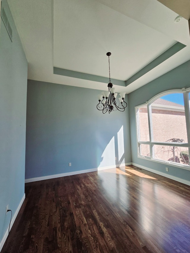 unfurnished dining area with baseboards, visible vents, a tray ceiling, and wood finished floors