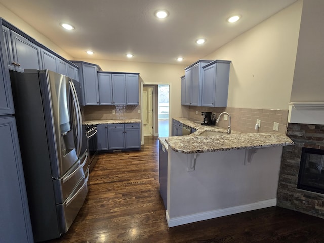 kitchen with dark wood finished floors, a peninsula, light stone countertops, stainless steel appliances, and a sink