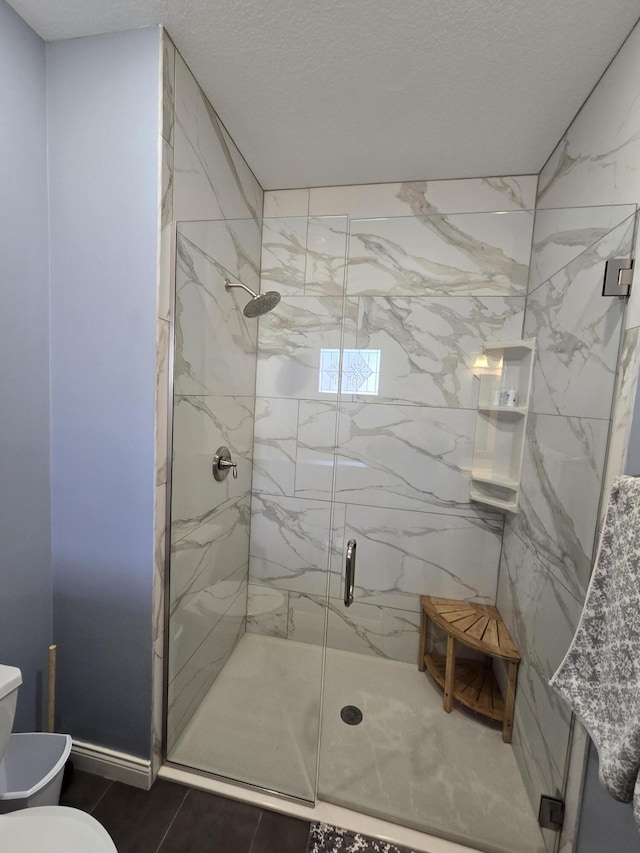 full bathroom featuring a marble finish shower, a textured ceiling, and toilet