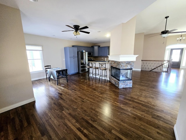 living area with a healthy amount of sunlight, dark wood finished floors, baseboards, and ceiling fan with notable chandelier