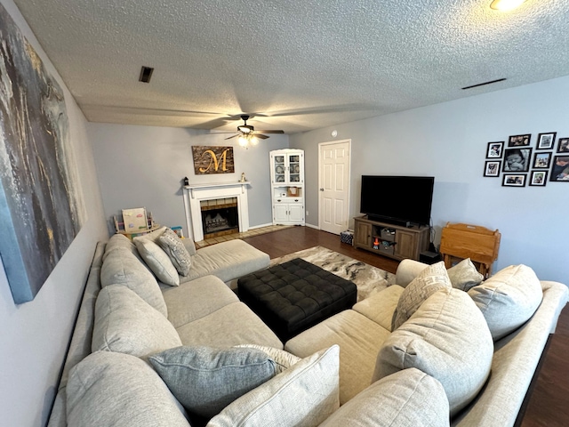 living area with a textured ceiling, visible vents, dark wood finished floors, and a tiled fireplace