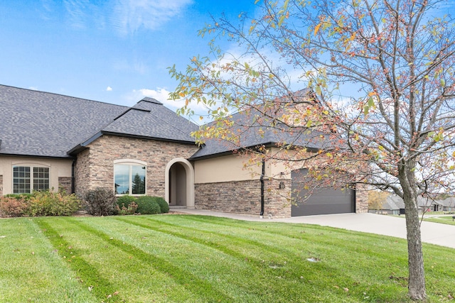 french country inspired facade featuring concrete driveway, a front lawn, a shingled roof, and stucco siding