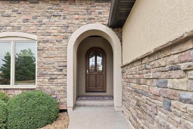 view of exterior entry featuring brick siding and stucco siding