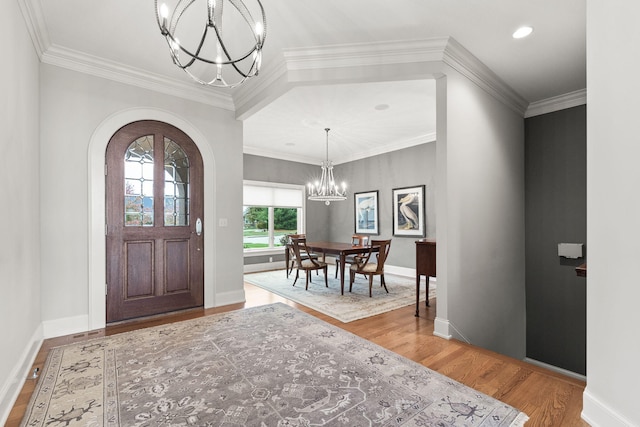 foyer featuring arched walkways, wood finished floors, crown molding, and an inviting chandelier