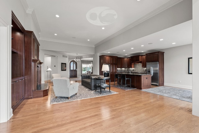 living area with baseboards, light wood finished floors, ornamental molding, and a notable chandelier