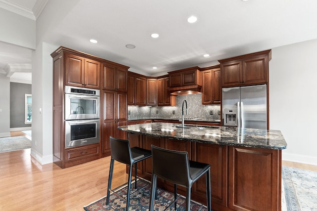 kitchen with light wood-style flooring, a breakfast bar, appliances with stainless steel finishes, decorative backsplash, and dark stone countertops