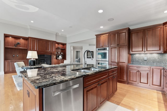 kitchen featuring stainless steel appliances, a sink, a kitchen island with sink, and light wood-style floors