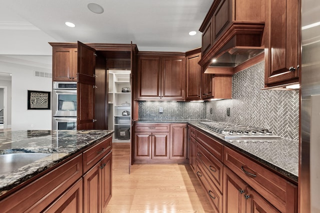 kitchen with dark stone counters, light wood-style flooring, appliances with stainless steel finishes, backsplash, and recessed lighting