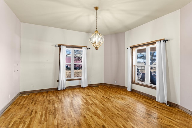 unfurnished room featuring a chandelier, light wood finished floors, and a wealth of natural light