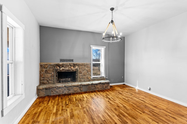 unfurnished living room with baseboards, a stone fireplace, an inviting chandelier, and wood finished floors