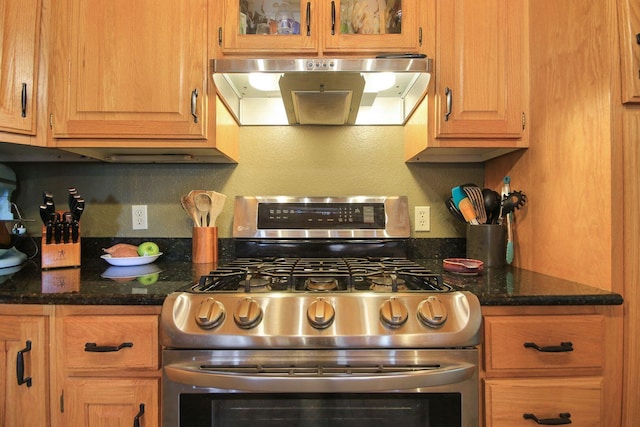 kitchen with wall chimney exhaust hood, dark stone countertops, and stainless steel range with gas stovetop