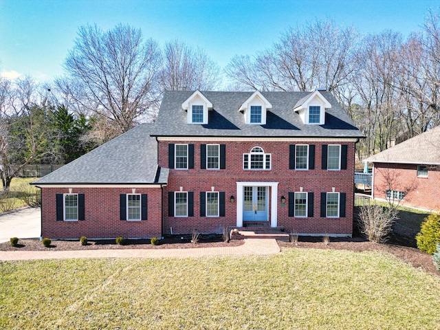 view of front of house with brick siding, a shingled roof, a front lawn, and french doors