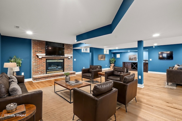 living room with a brick fireplace, wood finished floors, visible vents, and baseboards