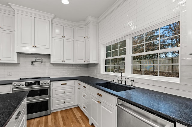 kitchen with dark countertops, appliances with stainless steel finishes, crown molding, white cabinetry, and a sink