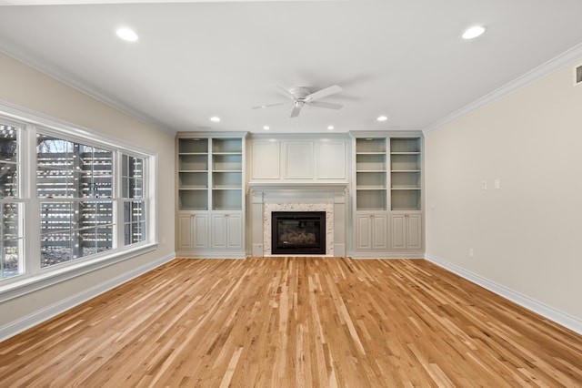 unfurnished living room with plenty of natural light, a glass covered fireplace, crown molding, and baseboards