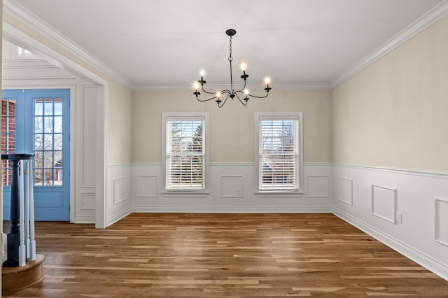 unfurnished dining area with a notable chandelier, ornamental molding, wood finished floors, and wainscoting