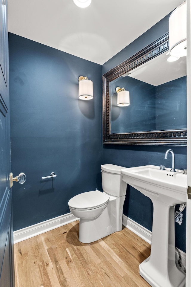 half bathroom with toilet, baseboards, and wood finished floors