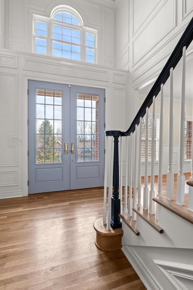 foyer with light wood-style flooring, a decorative wall, stairs, french doors, and ornamental molding