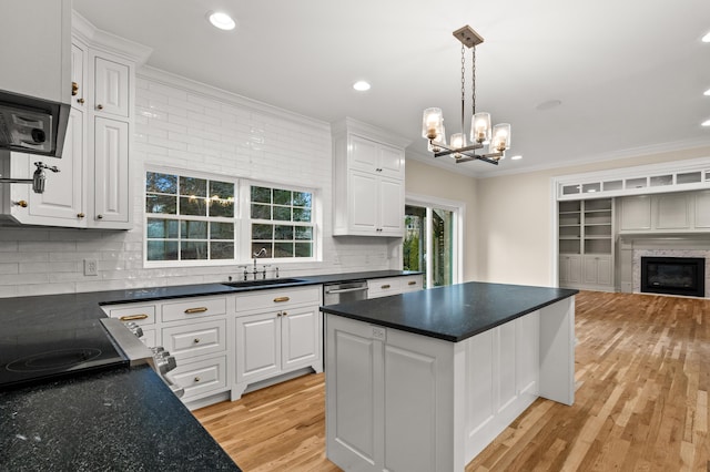 kitchen with dark countertops, ornamental molding, a glass covered fireplace, white cabinetry, and a sink