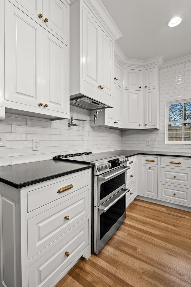 kitchen with range with two ovens, ornamental molding, light wood-style floors, white cabinetry, and backsplash