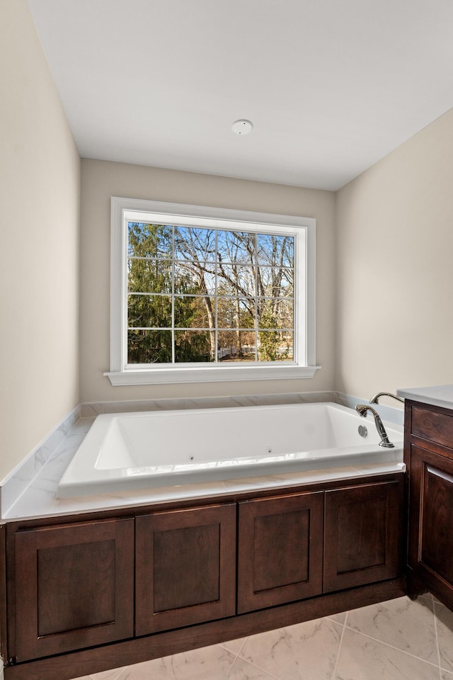 full bathroom featuring marble finish floor, plenty of natural light, a tub with jets, and vanity