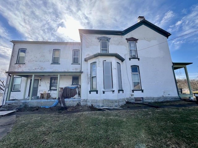 view of front of property featuring a porch, brick siding, a chimney, and a front lawn