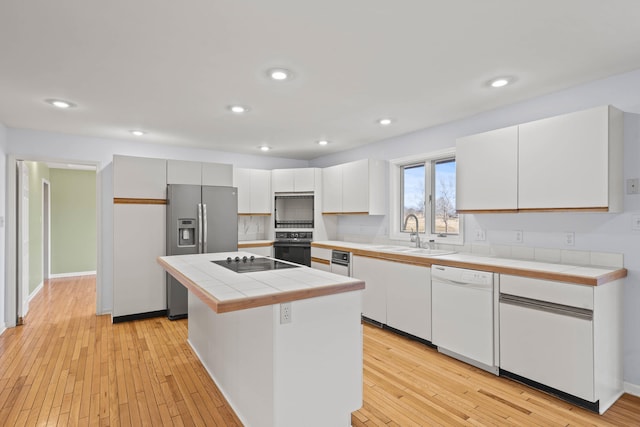 kitchen with tile counters, a center island, a sink, and black appliances