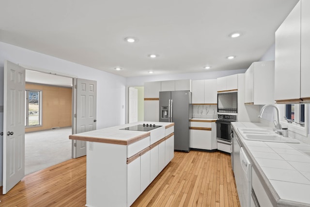 kitchen featuring a sink, white cabinets, tile counters, a center island, and black appliances