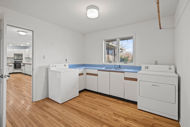 laundry area featuring light wood finished floors, cabinet space, washer and dryer, and a sink