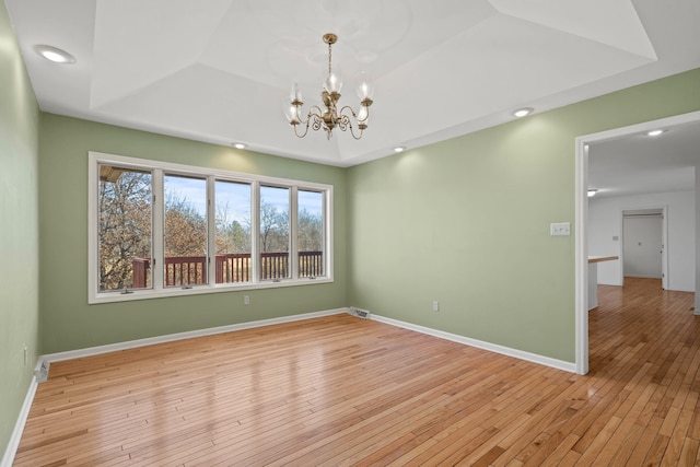 unfurnished room featuring baseboards, visible vents, a raised ceiling, light wood-type flooring, and a chandelier