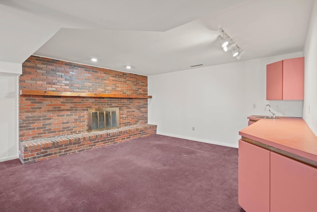 unfurnished living room with baseboards, rail lighting, carpet floors, a brick fireplace, and a sink