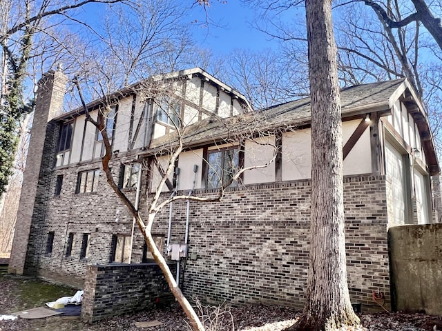 view of side of property featuring brick siding, a chimney, and stucco siding