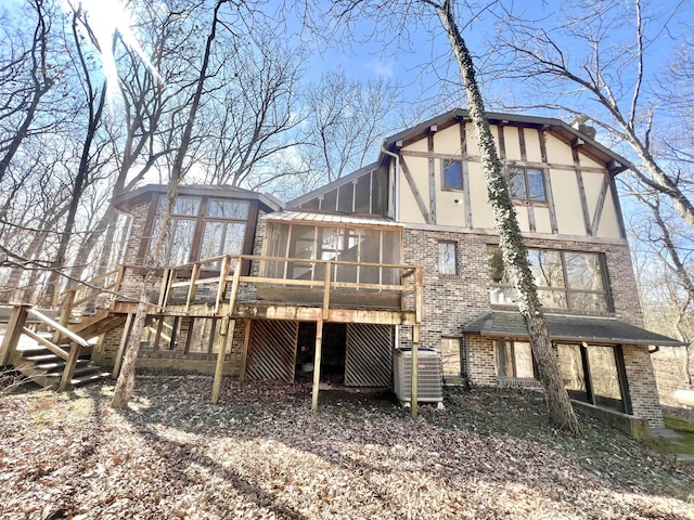 back of house featuring brick siding, central AC unit, a sunroom, stairs, and stucco siding