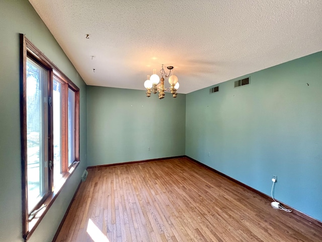 unfurnished room with baseboards, visible vents, an inviting chandelier, and wood finished floors