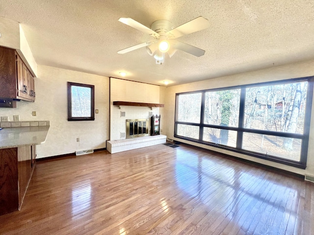 unfurnished living room with a brick fireplace, plenty of natural light, visible vents, and dark wood-style flooring